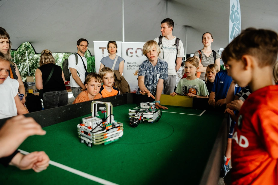 LNDW 2026: Kinder beobachten Lego-Roboterfahrzeuge auf einem Tischkicker-Feld