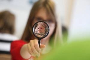 A girl looks through a magnifying glass.